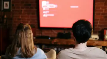 Casal sentado no sofá assistindo televisão juntos, representando momentos de entretenimento em casa